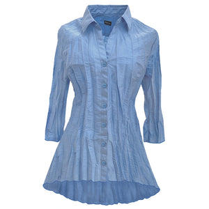 The blouse has a classic collar and 3/4 flair sleeves. It  has a tunic shape with more length in the back. The color Sky can be described as a soft light blue with a hint of yellow, inspired by the daytime sky. The buttons are of the same color.